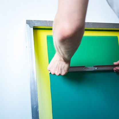 A photo of someone scraping green paint over a yellow screen to make a screen print.