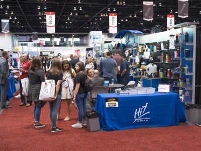 A photo of people at a trade show, standing next to a table with a blue tablecloth that says Hit.