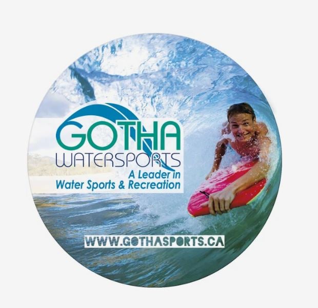An ad for Gotha Watersports, showing a photo of someone lying on a surfboard under a wave, next to contact info, printed on a circular magnet.