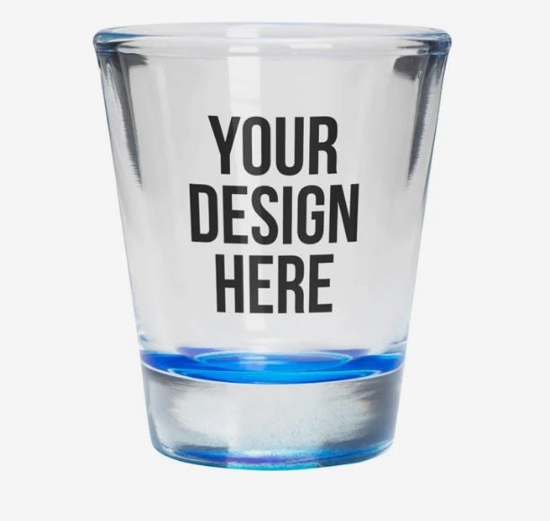 A photo of a clear shot glass with a blue bottom and with YOUR DESIGN HERE printed on it.