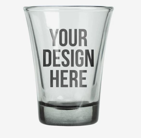 A photo of a shot glass with a black bottom and with YOUR DESIGN HERE printed on it.