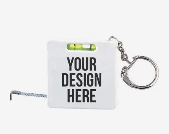 A photo of a white square tape measure keychain with a spirit level, and YOUR DESIGN HERE printed in black.