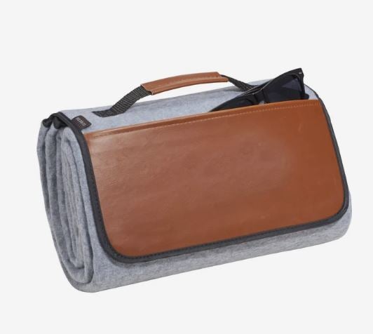 A photo of a folded grey picnic blanket with a brown flap and handle.