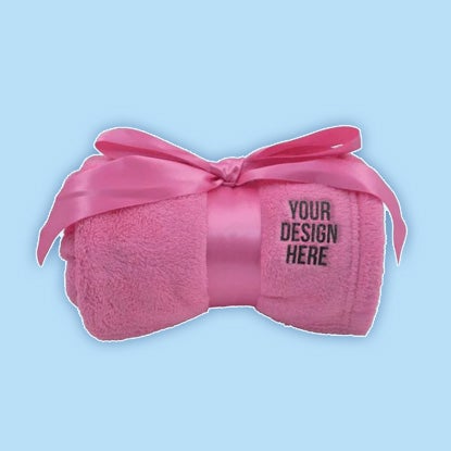 Rolled pink fleece blanket tied with a matching satin bow, with black 'YOUR DESIGN HERE' text on the front.
