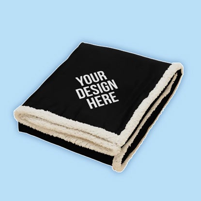 Folded black blanket with cream sherpa lining and white 'YOUR DESIGN HERE' text on the front.