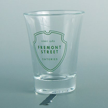 A photo of a shot glass with a green shield print design.