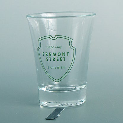 A photo of a shot glass with a green shield print design.