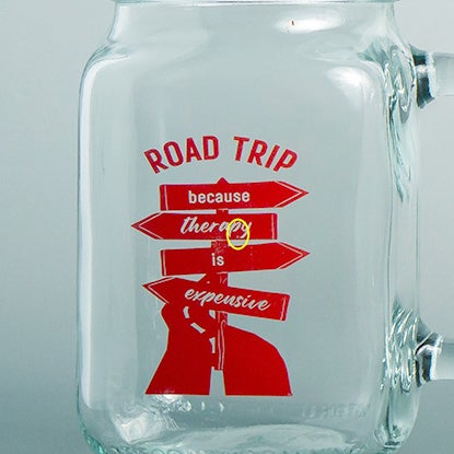 A photo showing a close-up of the damage on a red screen print a glass mason jar. The design is a red road and road sign, and ROAD TRIP in red.