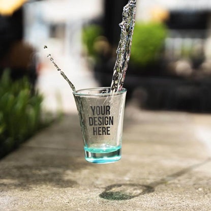 A photo of a falling shot glass with water splashing out of it.