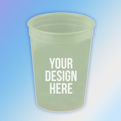 A photo of a pale green glow-in-the-dark plastic cup with YOUR DESIGN HERE printed on the front. It's on a blue background.