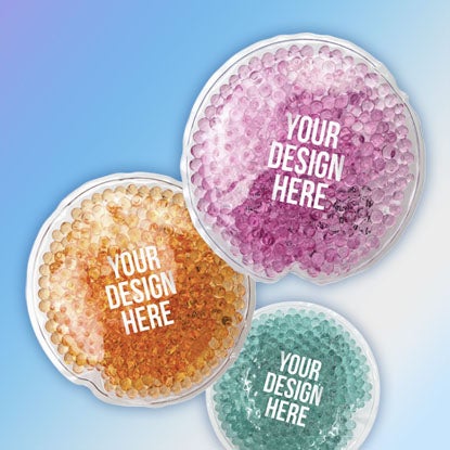A photo showing a hot/cold pack in three different colors - orange, pink, and green - all with YOUR DESIGN HERE printed on the front.