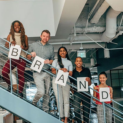 A photo showing five people lined up on stairs, each holding a letter to spell out the word brand.