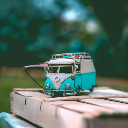 A photo showing a mini retro campervan with a garden out of focus in the background.