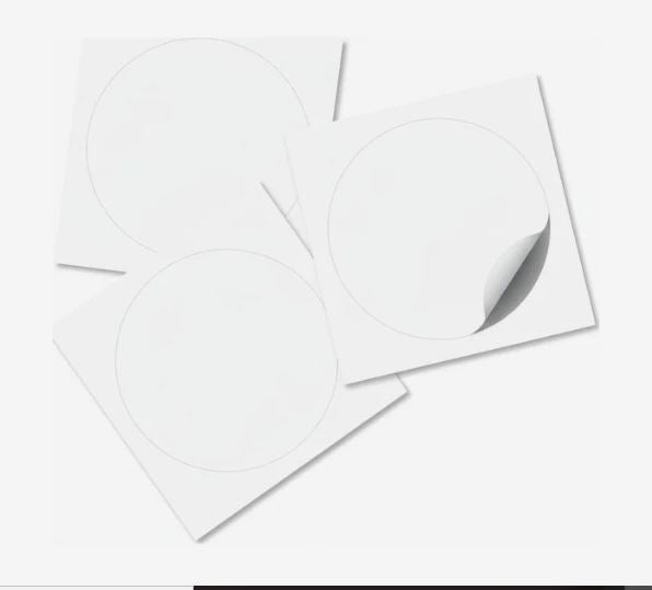 Three blank white circular peel-and-stick labels on square backing sheets, with one sticker partially peeled away.