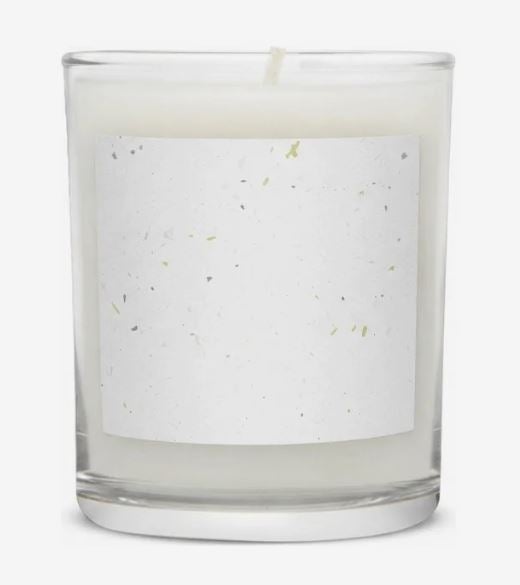 White wax candle in a clear glass jar with a single wick and a blank white rectangular label featuring small colored flecks.