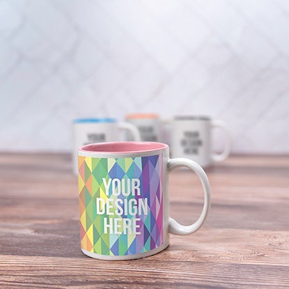 A photo of a mug with a rainbow geometric print, with pink inside, and YOUR DESIGN HERE printed on the front.