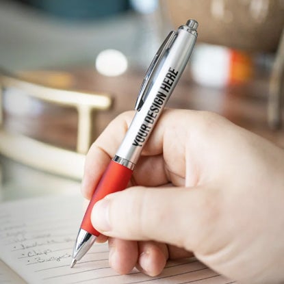 A photo showing a hand holding a green pen, resting on a wooden table.