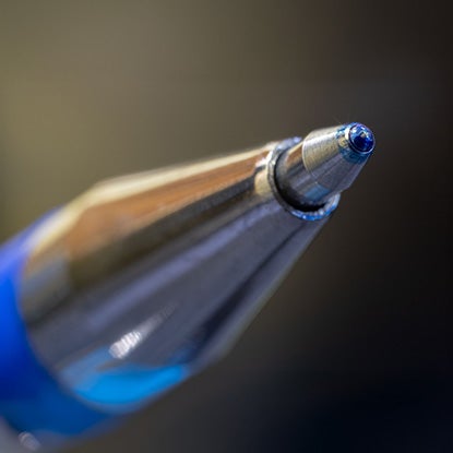 A close-up of a ballpoint pen tip with ink on the end.