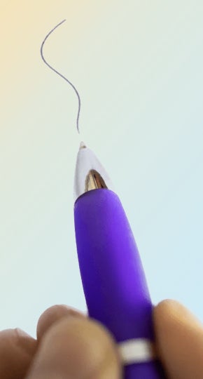 A close-up photo of someone holding a purple pen and drawing a black squiggly line.