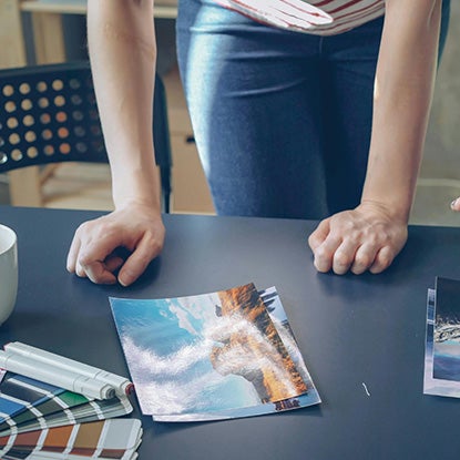A photo of the lower half of a person as they bend over a table, looking at a photo of a landscape.