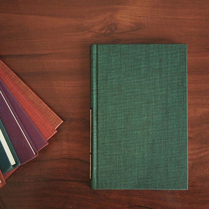 A photo showing a hardback notebook with a textile cover resting on a dark wooden desk.