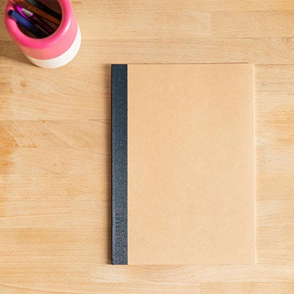 A photo showing a stack of wire-o notebooks sitting on a pale wood table.