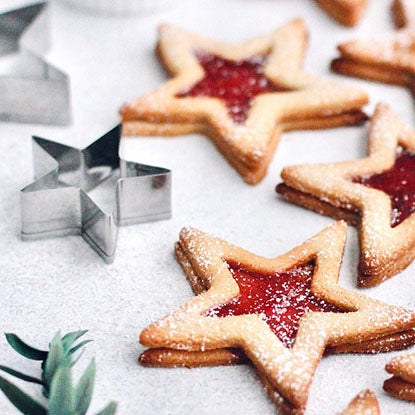 A photo of star-shaped jam-filled cookies next to the stainless steel cookie cutter used to make them.